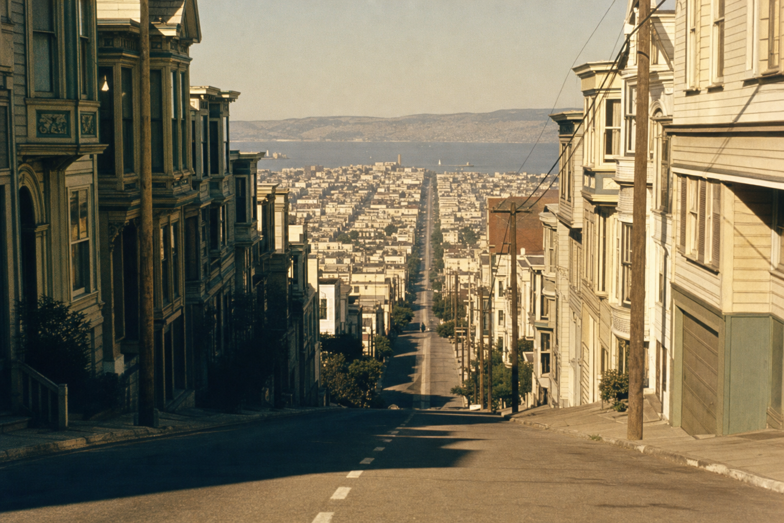 A steep San Francisco residential street in 1968 plunging towards the bay, Victorian houses flanking both sides